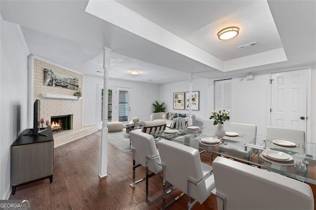 interior space with a fireplace, visible vents, a tray ceiling, and wood finished floors