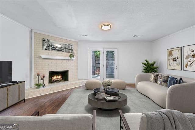 living area featuring visible vents, ornamental molding, a brick fireplace, and wood finished floors