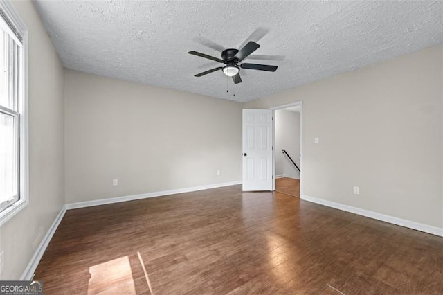 empty room with a textured ceiling, wood finished floors, ceiling fan, and baseboards
