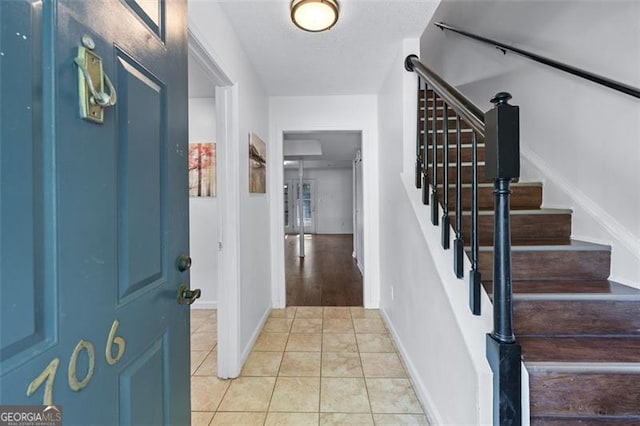 foyer featuring light tile patterned flooring, baseboards, and stairs