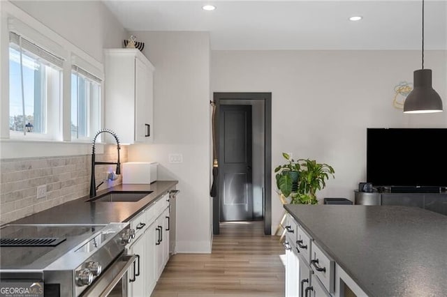 kitchen with tasteful backsplash, dark countertops, appliances with stainless steel finishes, light wood finished floors, and a sink