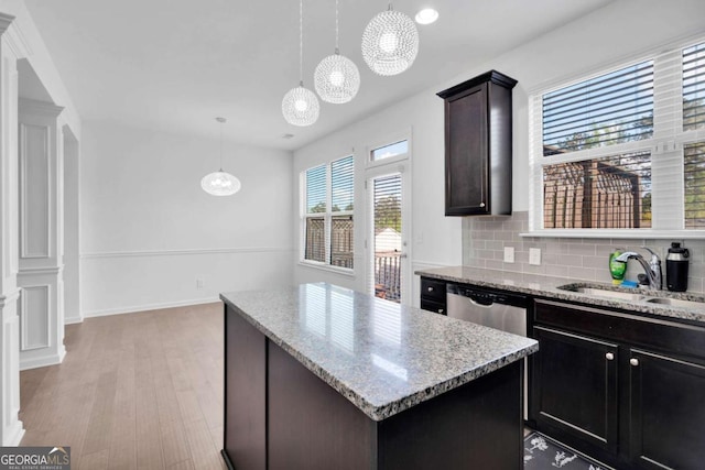 kitchen with light wood-type flooring, a kitchen island, light stone countertops, dishwasher, and a sink
