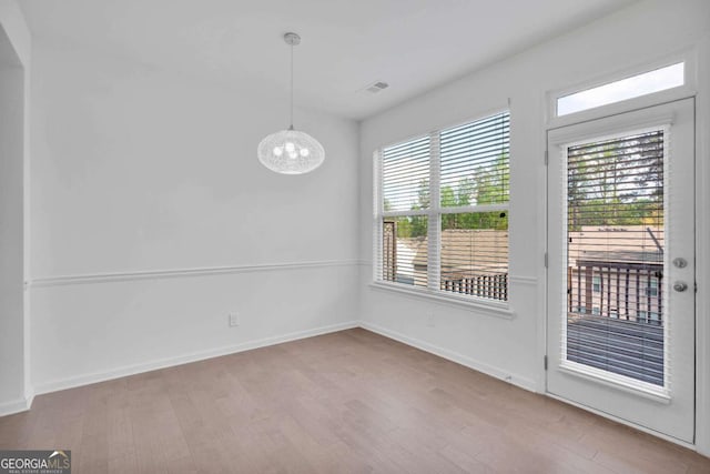 unfurnished dining area with wood finished floors, a notable chandelier, and baseboards