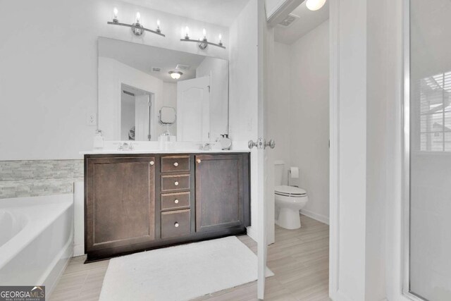 bathroom with double vanity, toilet, a bath, visible vents, and a sink