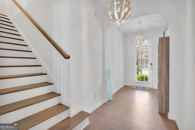 foyer featuring stairway, baseboards, an inviting chandelier, and wood finished floors