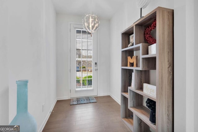 doorway to outside with a chandelier, wood finished floors, and baseboards