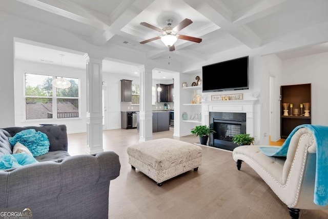 living room with decorative columns, light wood-type flooring, a ceiling fan, a glass covered fireplace, and coffered ceiling