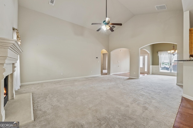 unfurnished living room featuring arched walkways, a ceiling fan, a lit fireplace, a chandelier, and high vaulted ceiling