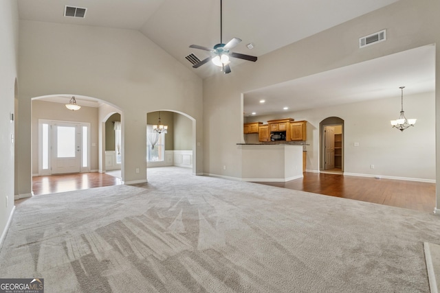 unfurnished living room with carpet flooring, a chandelier, a ceiling fan, arched walkways, and high vaulted ceiling