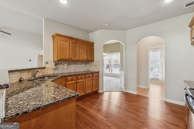 kitchen featuring a sink, brown cabinetry, arched walkways, tasteful backsplash, and dark stone countertops