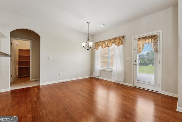 unfurnished dining area featuring arched walkways, a chandelier, wood finished floors, and baseboards