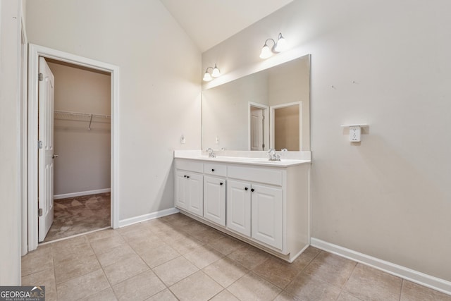 bathroom with tile patterned floors, double vanity, baseboards, a spacious closet, and high vaulted ceiling