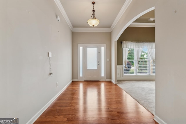 foyer featuring crown molding, wood finished floors, arched walkways, and baseboards