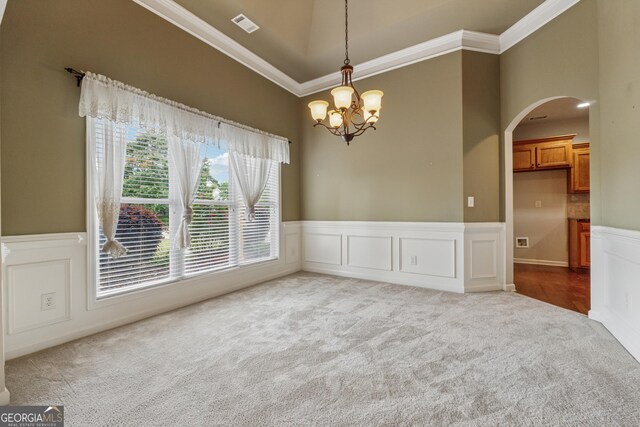 spare room with carpet flooring, crown molding, arched walkways, a chandelier, and a wainscoted wall