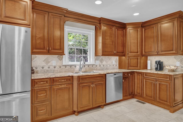 kitchen featuring light stone counters, backsplash, brown cabinetry, appliances with stainless steel finishes, and a sink