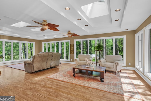 living area featuring recessed lighting, a ceiling fan, light wood-style floors, a tray ceiling, and a skylight