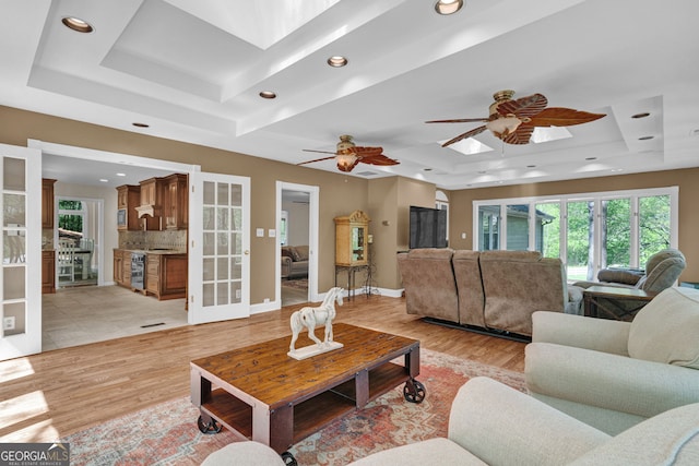 living area featuring a tray ceiling, a skylight, recessed lighting, and light wood-style flooring