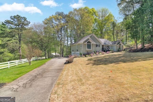 view of front of house featuring aphalt driveway, fence, and a front lawn