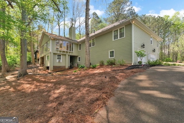 back of property featuring an attached garage, driveway, and a chimney