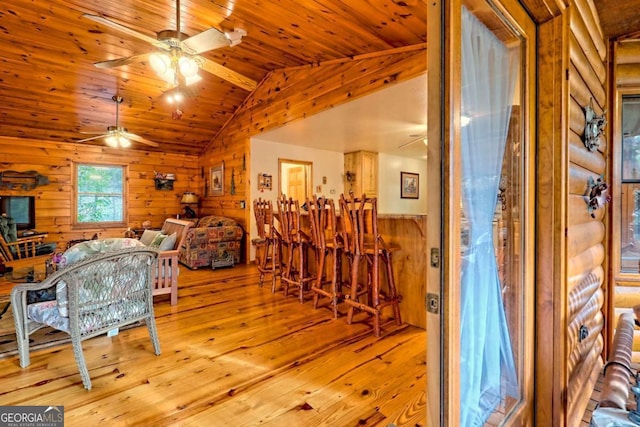 living area featuring a ceiling fan, hardwood / wood-style flooring, wood ceiling, wood walls, and lofted ceiling