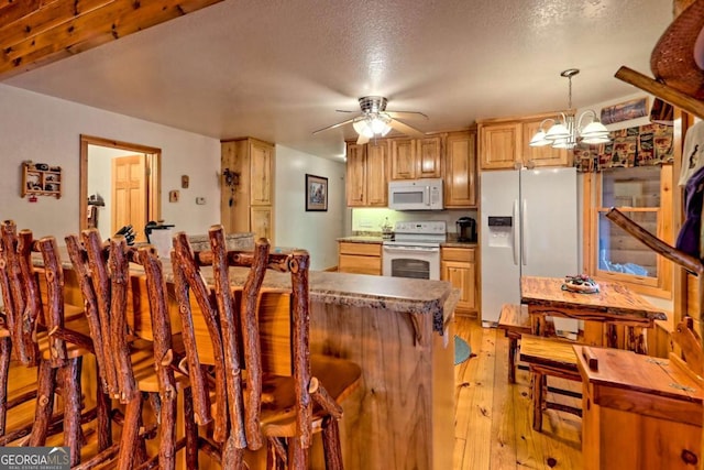 kitchen with white appliances, a kitchen bar, a textured ceiling, light wood-style floors, and ceiling fan with notable chandelier