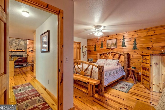 bedroom featuring a stone fireplace, light wood-style flooring, a textured ceiling, and wooden walls