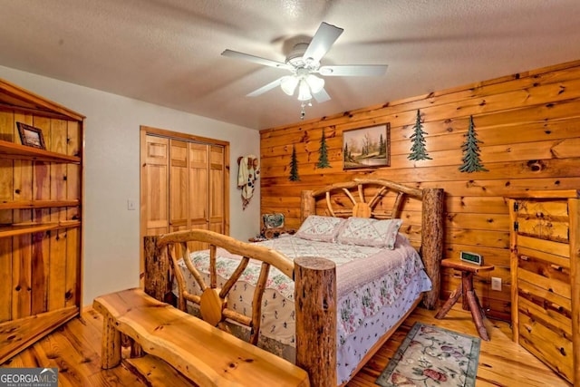 bedroom featuring wood walls, light wood-type flooring, a textured ceiling, and a ceiling fan