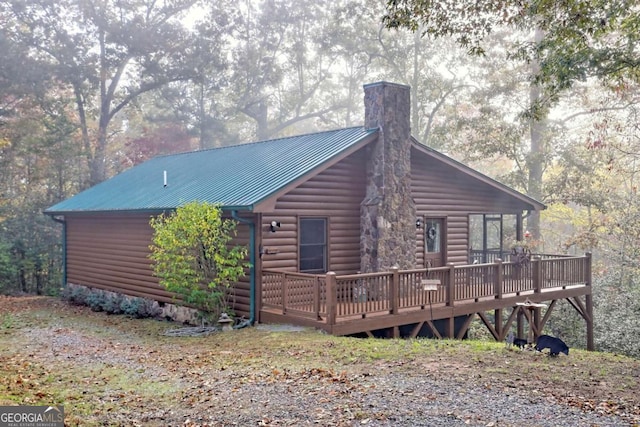exterior space with a chimney, a wooden deck, metal roof, and log veneer siding