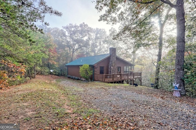 view of property exterior with a deck, a forest view, a chimney, and faux log siding