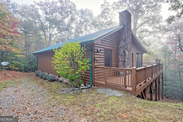 view of side of home with a chimney, faux log siding, crawl space, a deck, and metal roof
