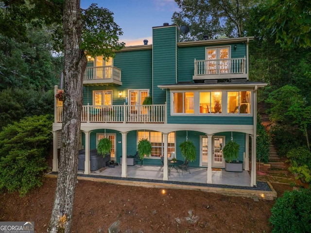 back of property at dusk with a chimney, french doors, a patio area, and a balcony