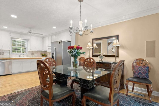 dining space with a textured ceiling, ceiling fan with notable chandelier, light wood finished floors, and visible vents