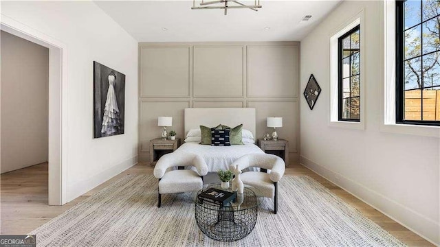 bedroom with a decorative wall, visible vents, light wood-style flooring, and multiple windows