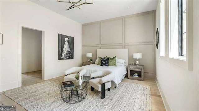bedroom featuring light wood-type flooring, a decorative wall, and an inviting chandelier