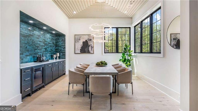 dining area featuring indoor bar, baseboards, light wood-type flooring, and beverage cooler