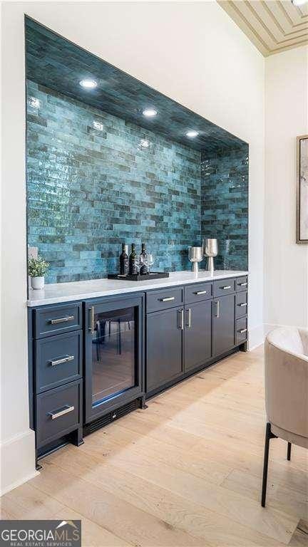 bar with backsplash, a dry bar, light wood finished floors, and beverage cooler