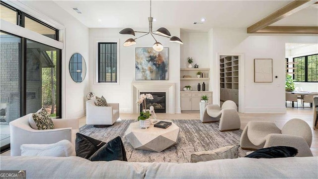 living room featuring visible vents, baseboards, a notable chandelier, wood finished floors, and a glass covered fireplace