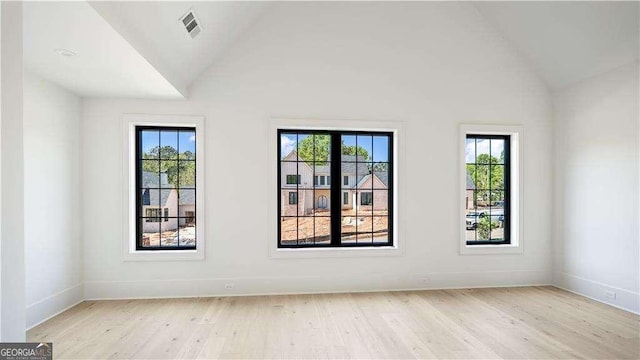 unfurnished room featuring visible vents, a wealth of natural light, light wood-style floors, and vaulted ceiling