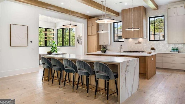 kitchen featuring light wood-style flooring, a large island, decorative backsplash, and beam ceiling