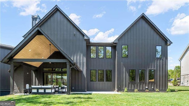 back of house with an outdoor living space, board and batten siding, a patio area, and a lawn