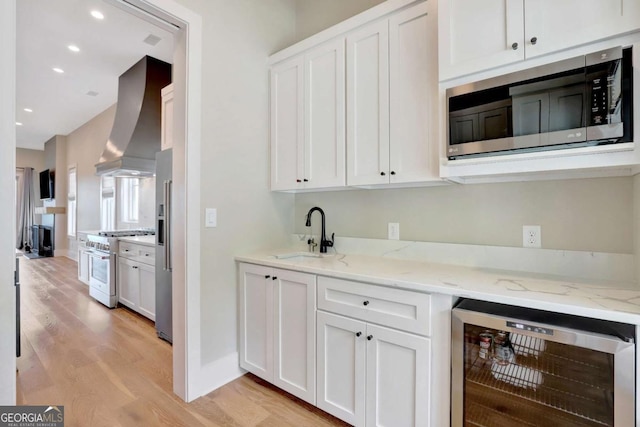 1130 Lupo Loop, Chattahoochee Hills, GA 30268 - kitchen featuring premium appliances, beverage cooler, wall chimney range hood, light wood-style floors, and white cabinets