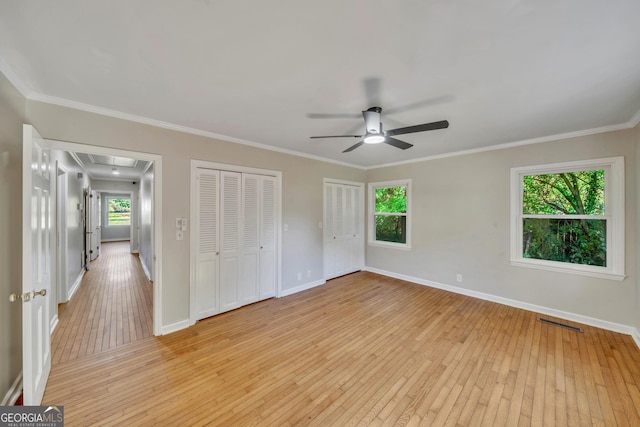 unfurnished bedroom featuring multiple closets, visible vents, light wood-type flooring, and attic access