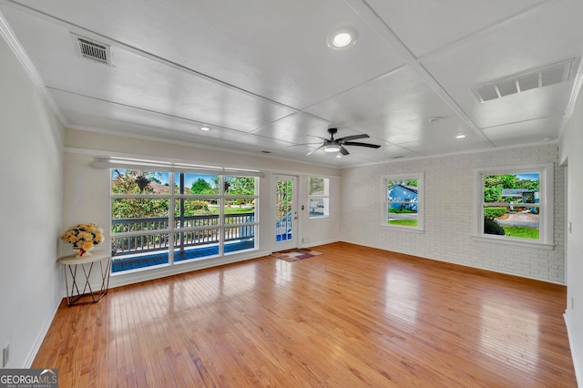 unfurnished living room with light wood-type flooring, baseboards, ornamental molding, brick wall, and a ceiling fan