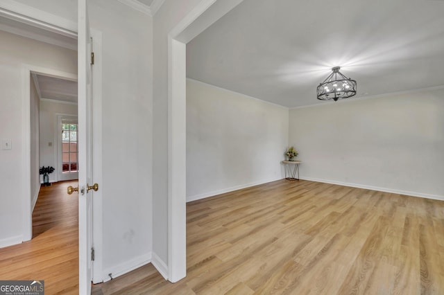empty room with a chandelier, crown molding, wood finished floors, and baseboards