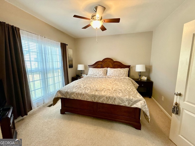 bedroom featuring a ceiling fan, light colored carpet, baseboards, and multiple windows