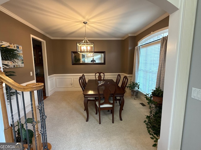 dining area with a chandelier, crown molding, light colored carpet, and wainscoting