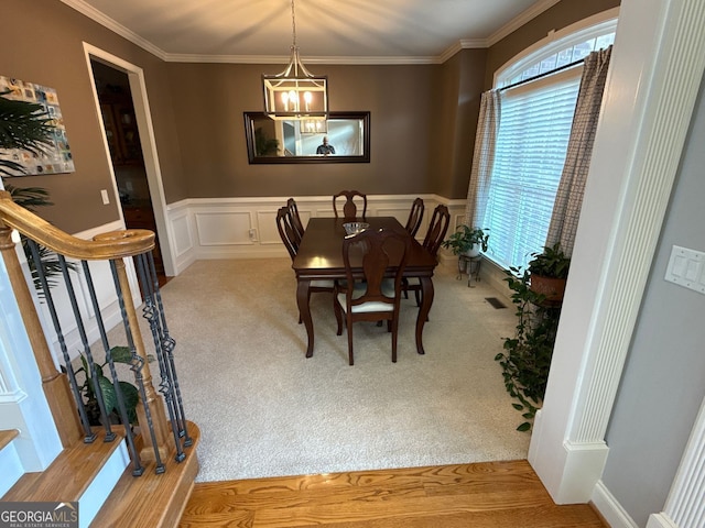 dining room with ornamental molding, wainscoting, an inviting chandelier, and light carpet