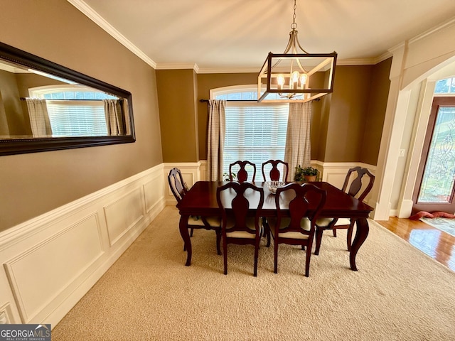 dining area featuring a decorative wall, a wainscoted wall, an inviting chandelier, and ornamental molding