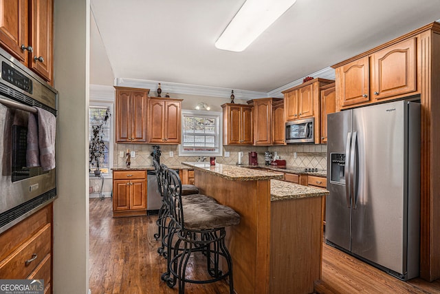 kitchen with light stone countertops, a kitchen breakfast bar, ornamental molding, a kitchen island, and appliances with stainless steel finishes
