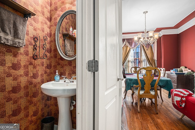 bathroom featuring ornamental molding, wood finished floors, an inviting chandelier, and wallpapered walls